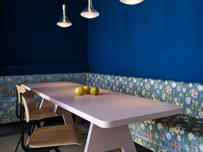 Eckbank und blaue Wand: Eckbank-Sitzgruppe mit floraler Sofa und blauer Akzentwand Hängelampen und Tageslicht für ein lebendiges Ambiente Kombination aus klassischen Möbeln und modernem Design
